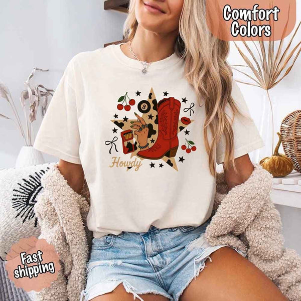 May include a short-sleeve comfort shirt with the phrase “Howdy Cowgirl” displayed in a bold Western-style font, featuring a star collage design with assorted colors for a playful and rustic look.