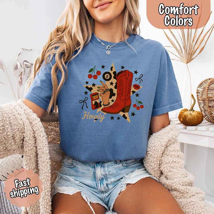 May include a short-sleeve comfort shirt with the phrase “Howdy Cowgirl” displayed in a bold Western-style font, featuring a star collage design with assorted colors for a playful and rustic look.