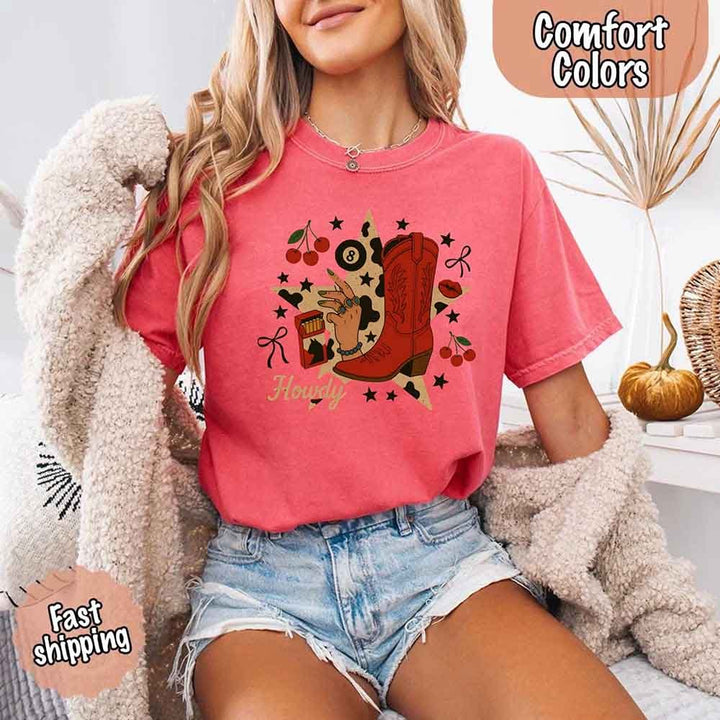 May include a short-sleeve comfort shirt with the phrase “Howdy Cowgirl” displayed in a bold Western-style font, featuring a star collage design with assorted colors for a playful and rustic look.
