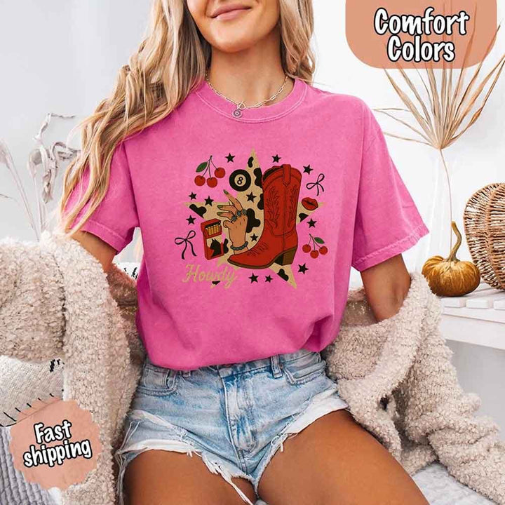 May include a short-sleeve comfort shirt with the phrase “Howdy Cowgirl” displayed in a bold Western-style font, featuring a star collage design with assorted colors for a playful and rustic look.